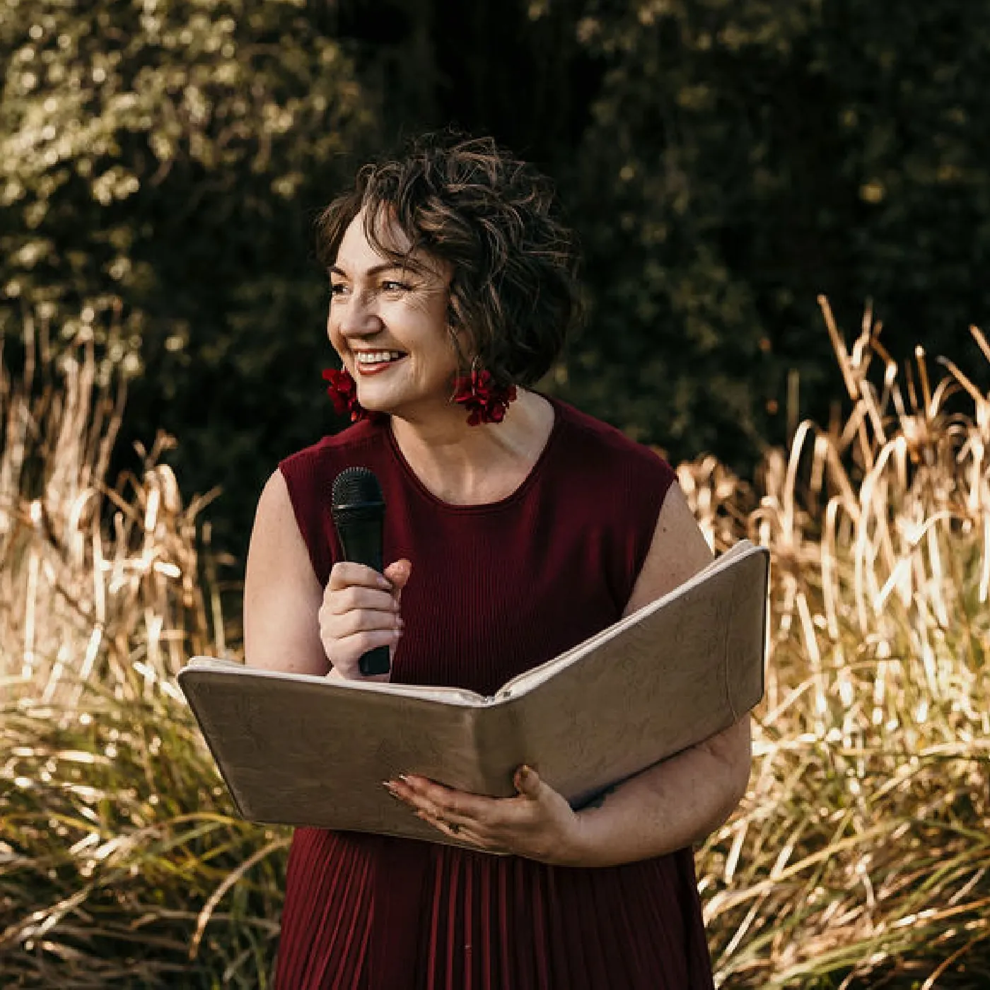 Lea-Anne, Christchurch wedding celebrant, holding her ceremony folder and microphone outdoors