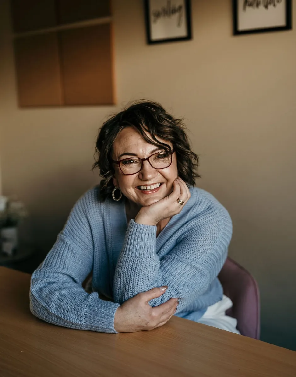 Lea-Anne, Christchurch marriage and civil union celebrant, smiling at a table in a blue jumper